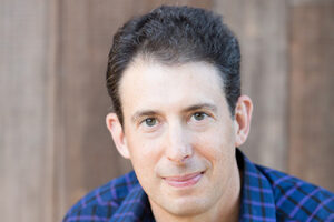 Headshot of Eric Klinenberg wearing a blue checked button down shirt.